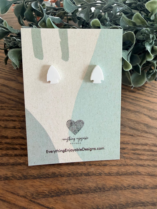 White acrylic arrowhead earrings on a branded card with a wooden surface and plant in the background